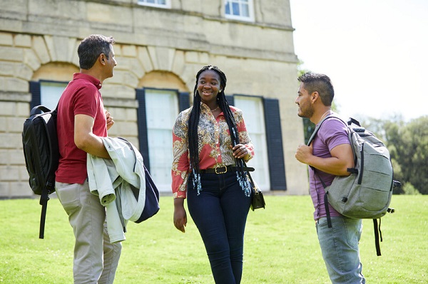 Postgraduate students standing chatting on lawn in front of university building.